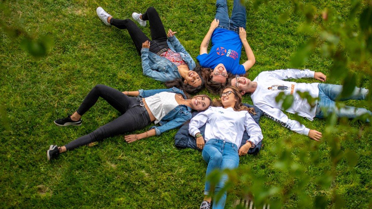 Students laying on the grass with their heads together in a star shape